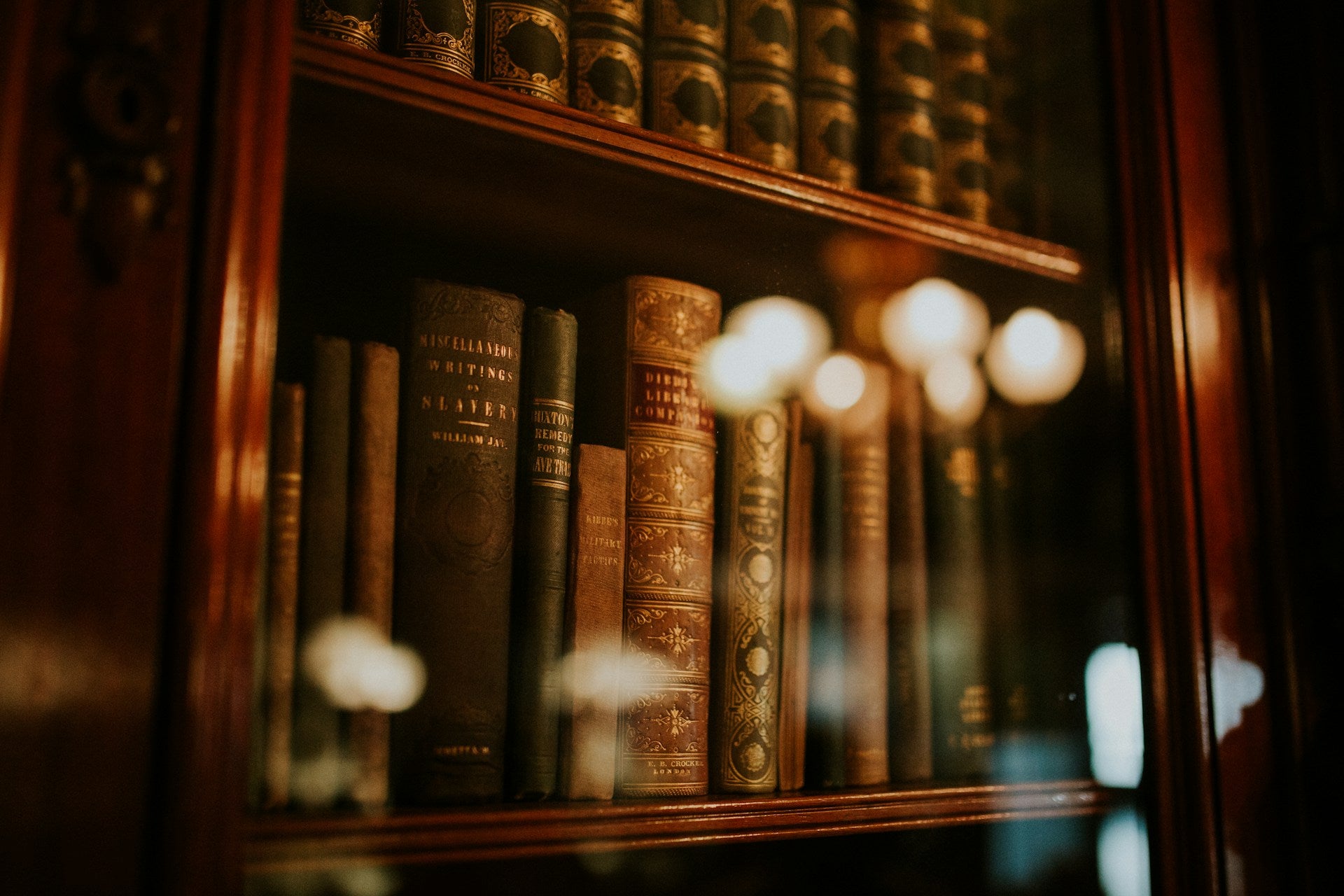 Old leather-bound and cloth-bound hardback books behind glass.