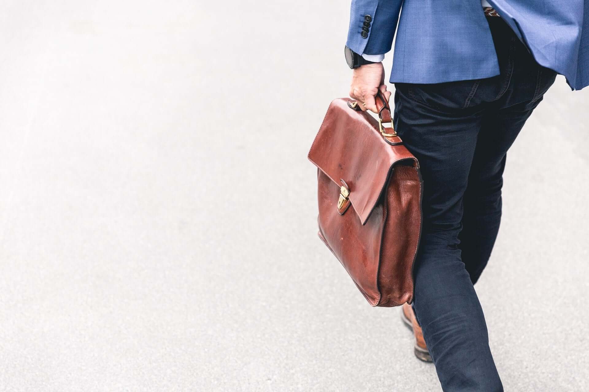 A rear shot of a man carrying a brown leather briefcase.