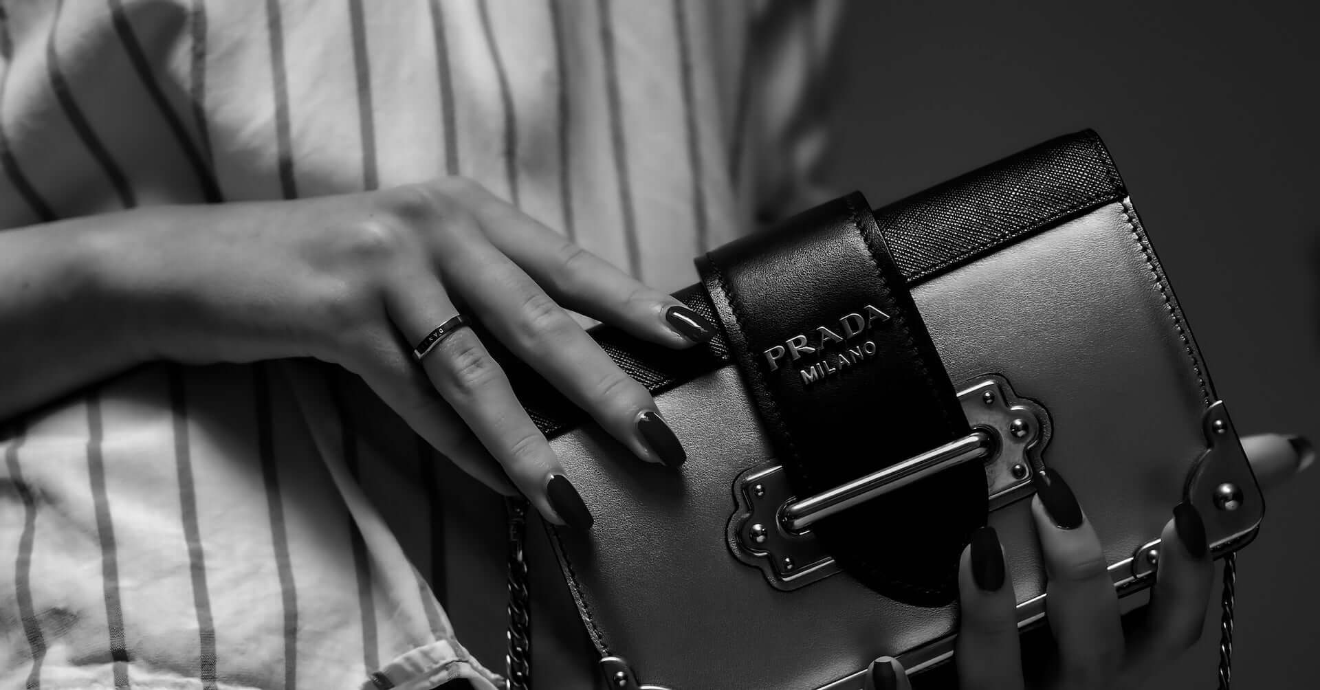 A black and white image of a woman holding a small Prada clutch purse.