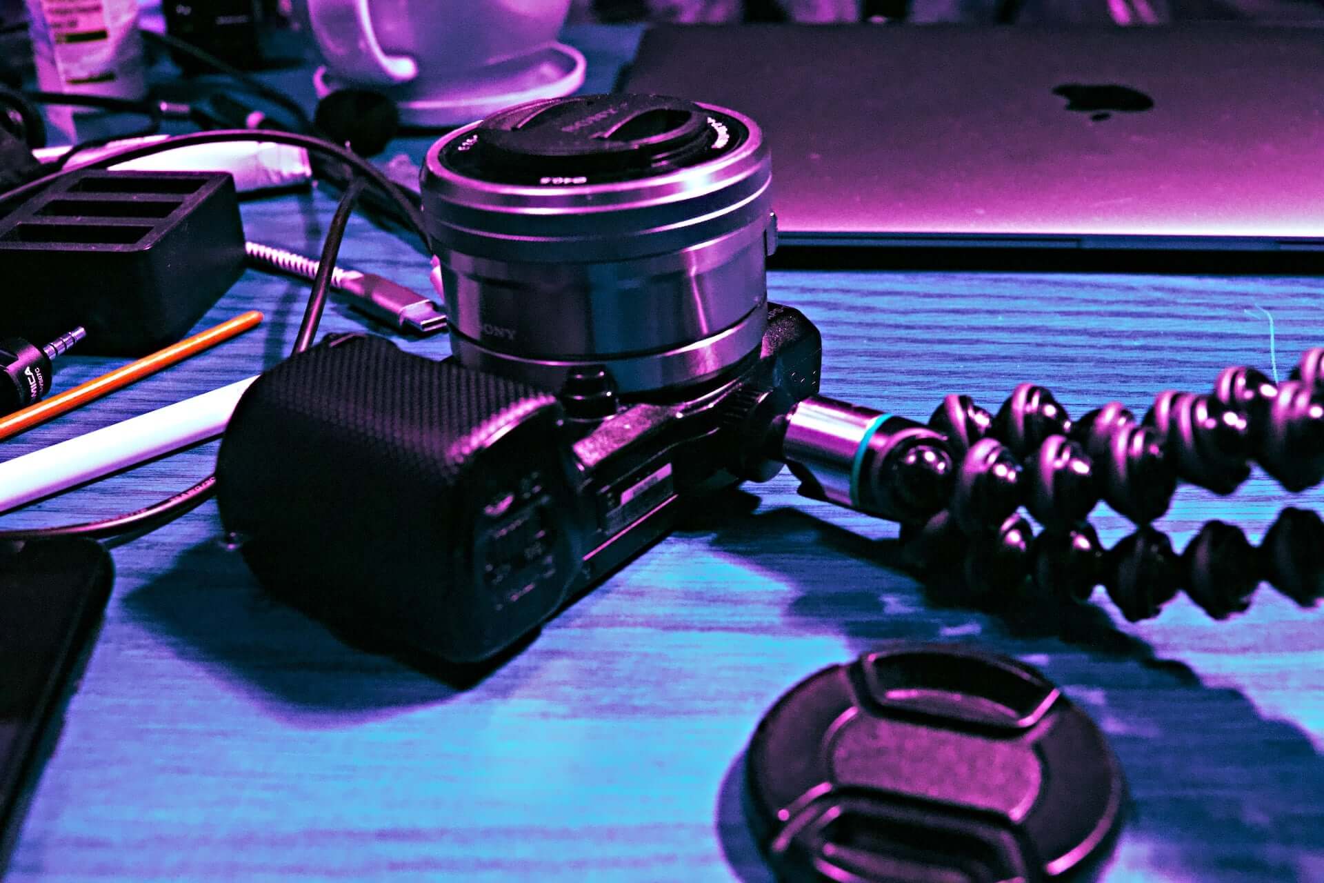 A camera on an adjustable tripod in pink and blue lighting.