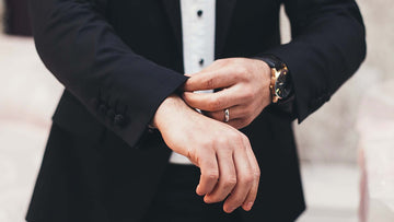 Close-up shot of a man in a black suit adjusting his wrist cuffs.