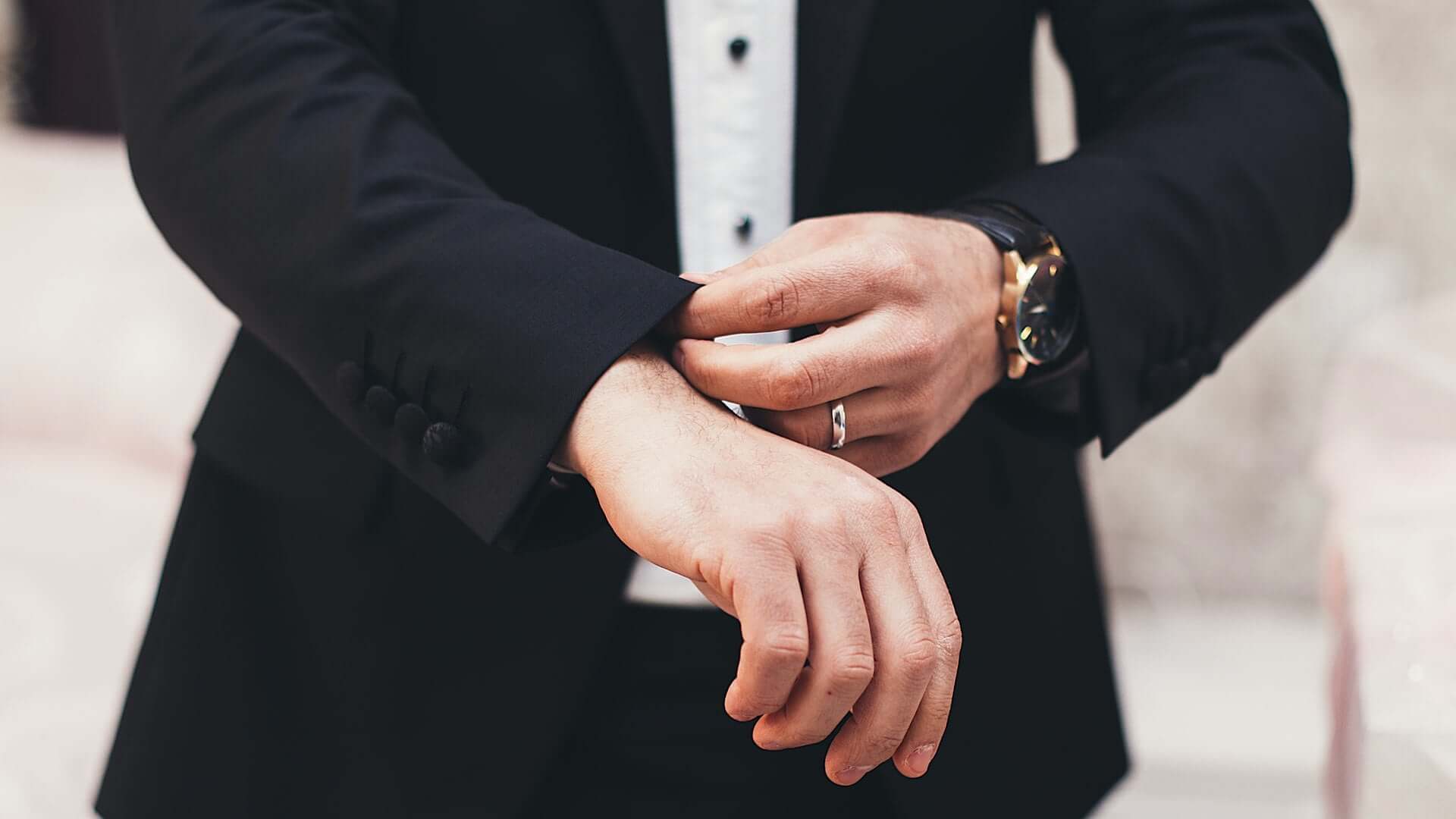 Close-up shot of a man in a black suit adjusting his wrist cuffs.