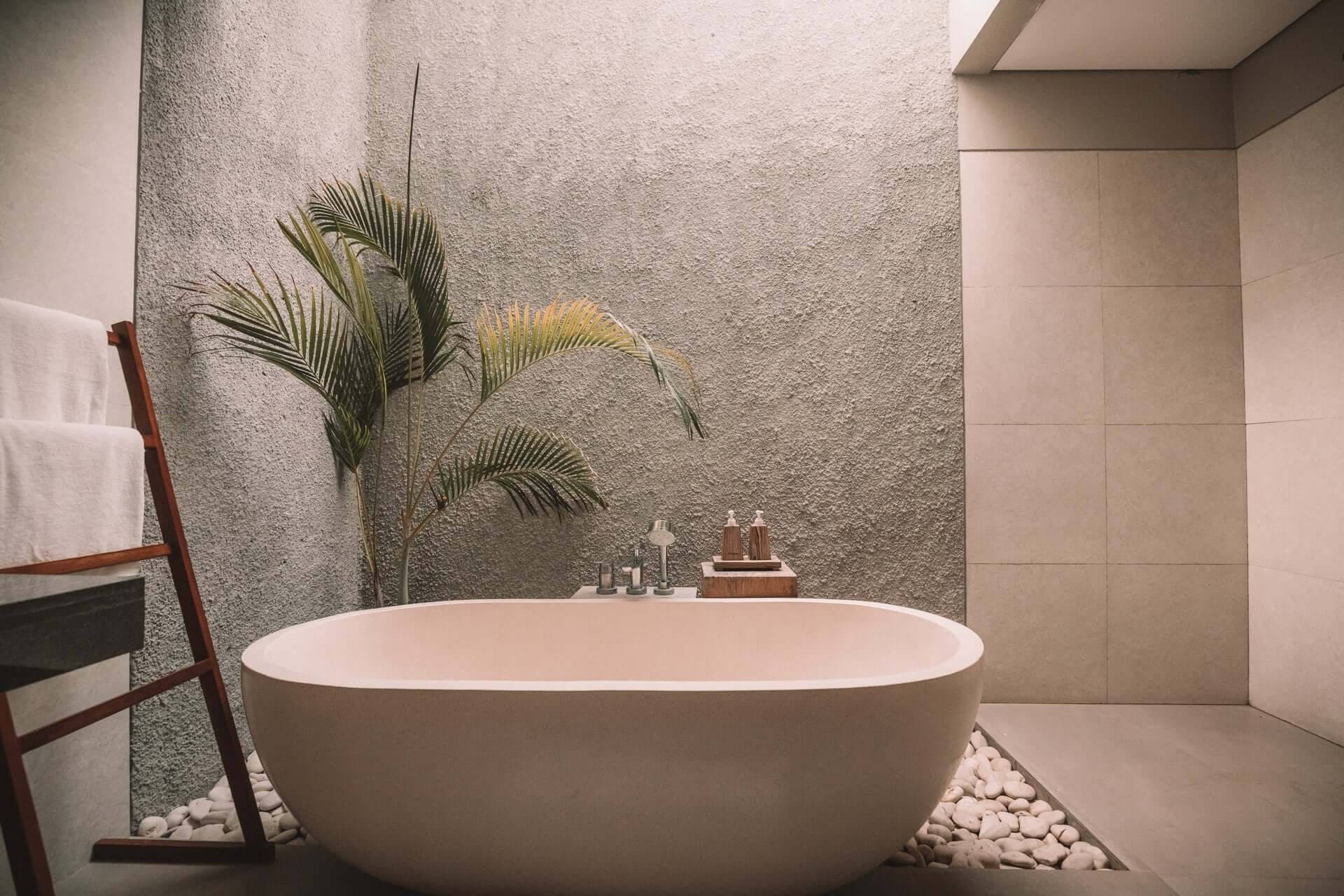 An earthtoned bathroom with an oval-shaped freestanding tub and a palm tree.