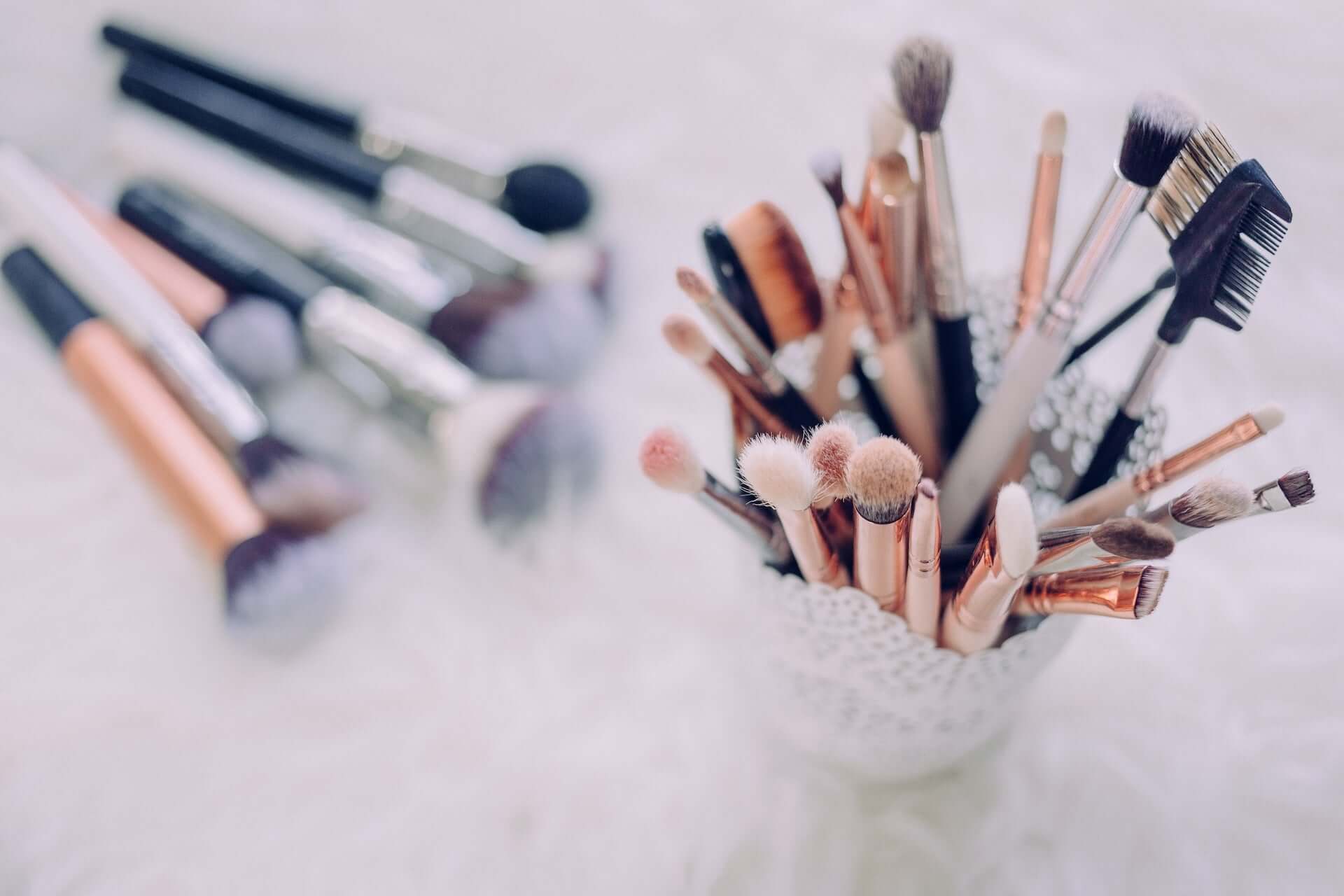 Various makeup brushes in a standing cup and laid out on a counter.