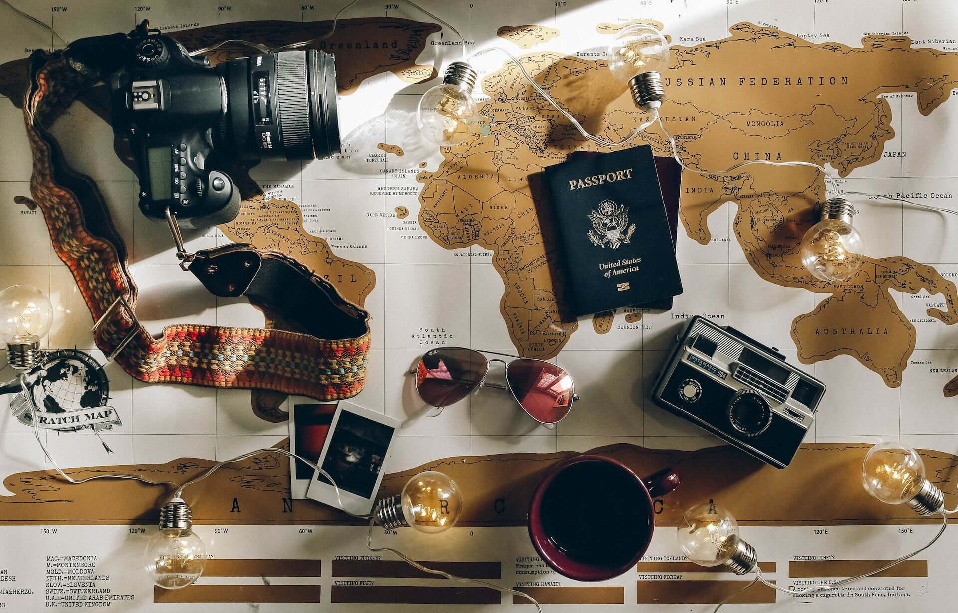 A scratch-off world map with cameras, a passport, and sunglasses resting on it.