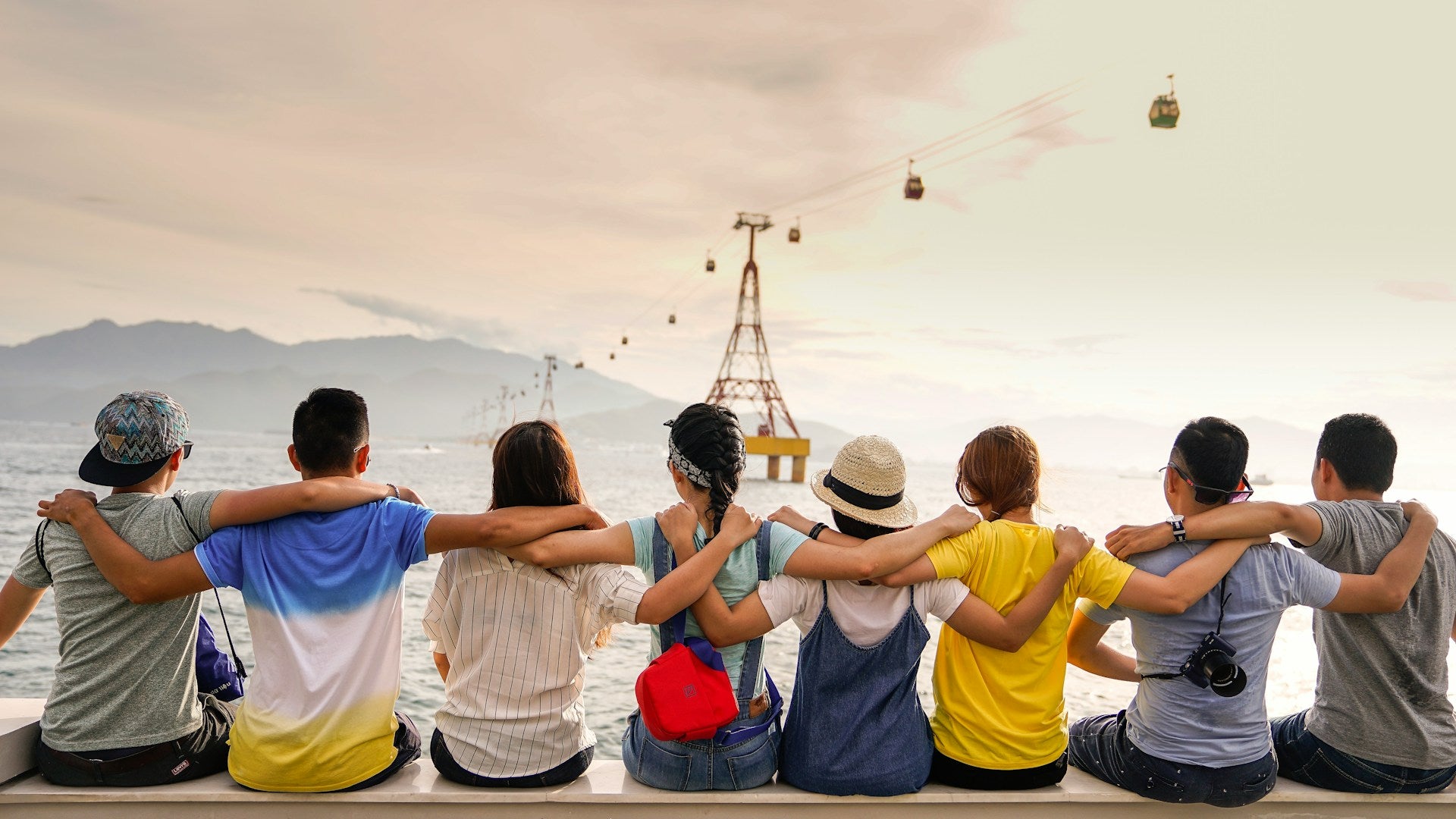 A line of people with their backs to the camera, sitting with thier arms around each other's shoulders.