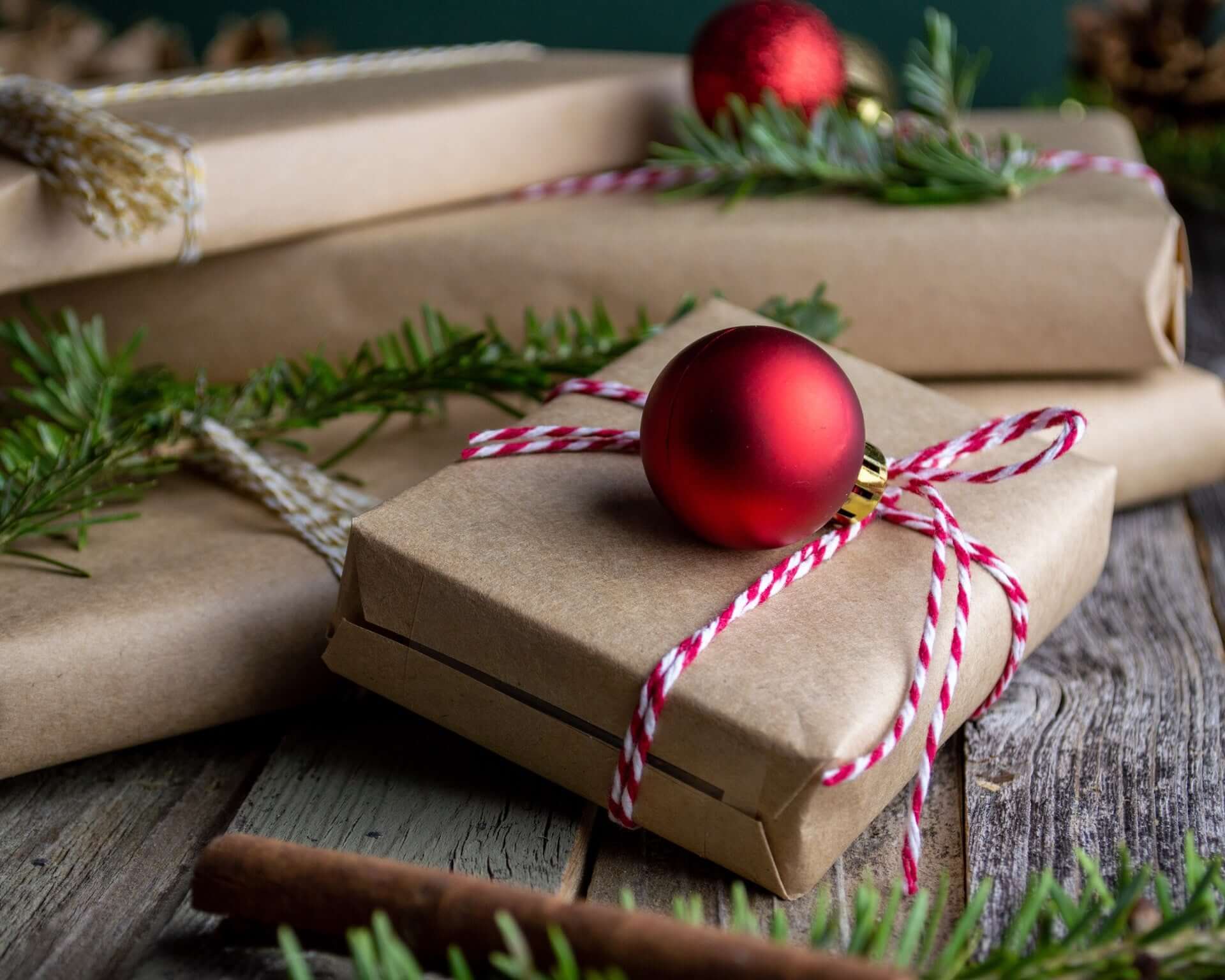 Brown paper wrapped presents with red and white string tied around them, decorated with red Christmas baubles.