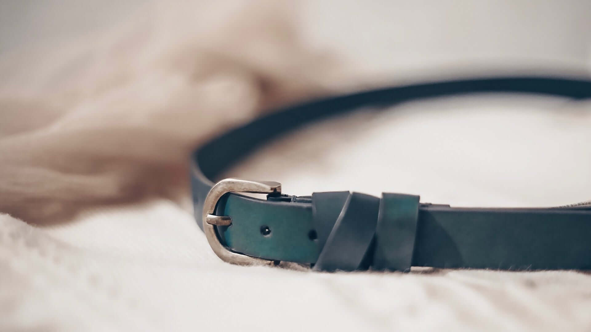 A blue leather belt on a white knit blanket.