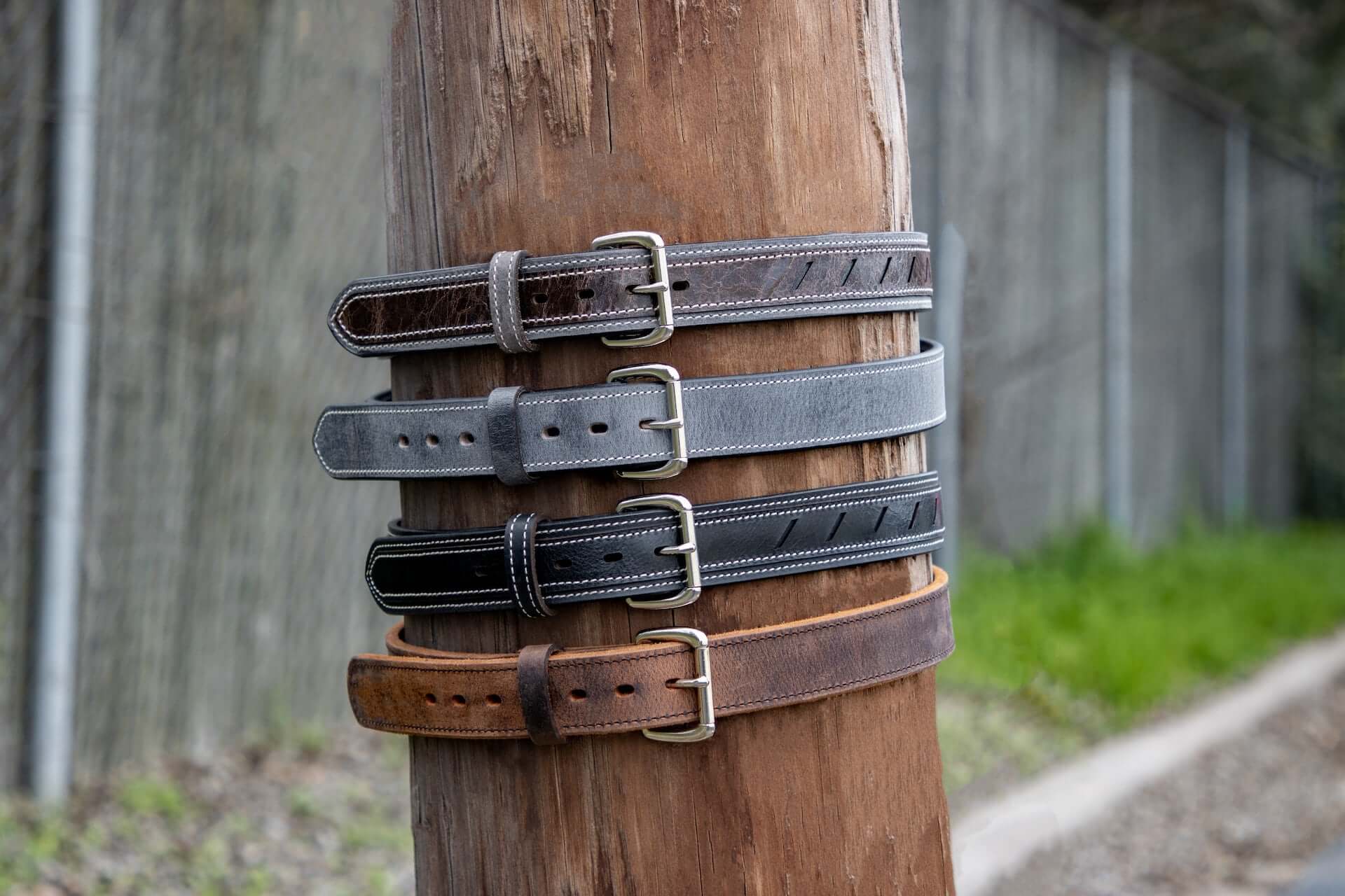 Four belts in various neutral colors fastened around a telephone pole.