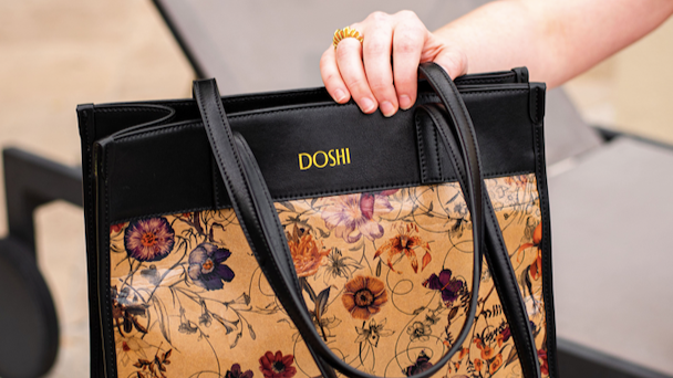 A floral tote bag with black accents and the brand name DOSHI in small font across the top.