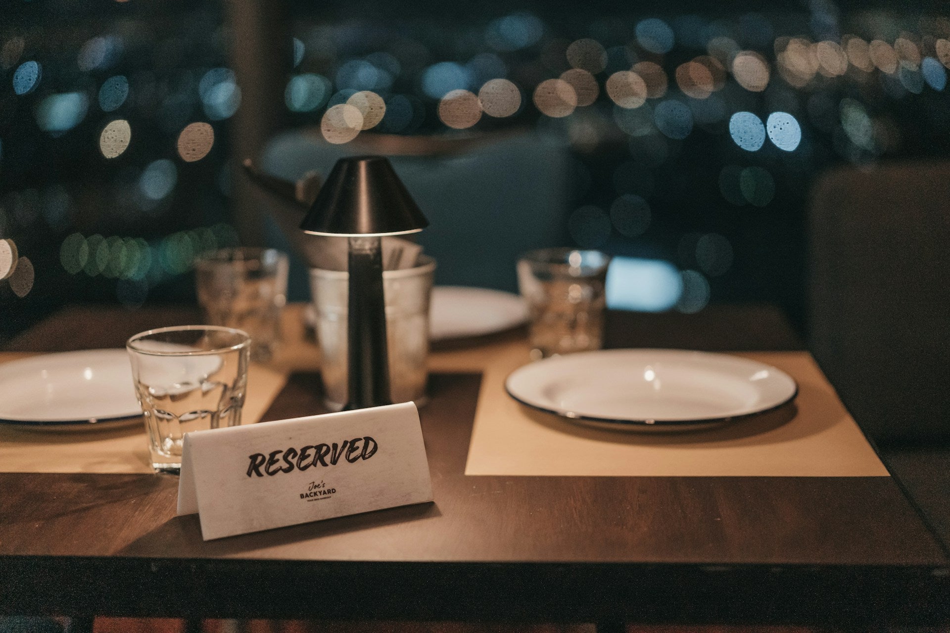 A table set for two with simple white dishes and a bottle of wine. A sign reads "Reserved."