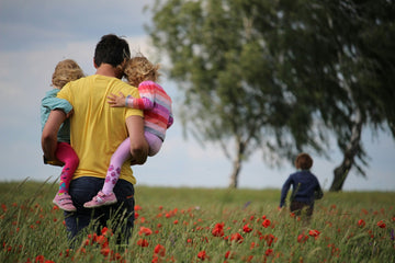 A man carrying two kids while following after a third.