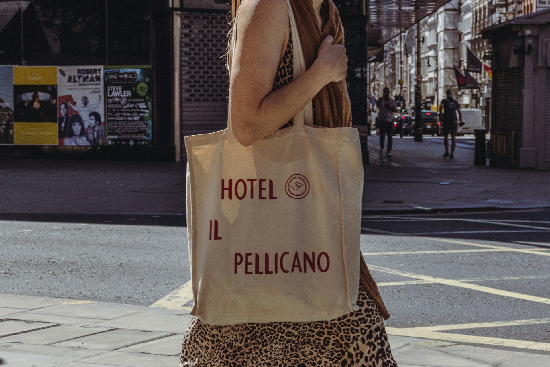 A woman carries a canvas tote bag that reads Hotel Il Pellicano.