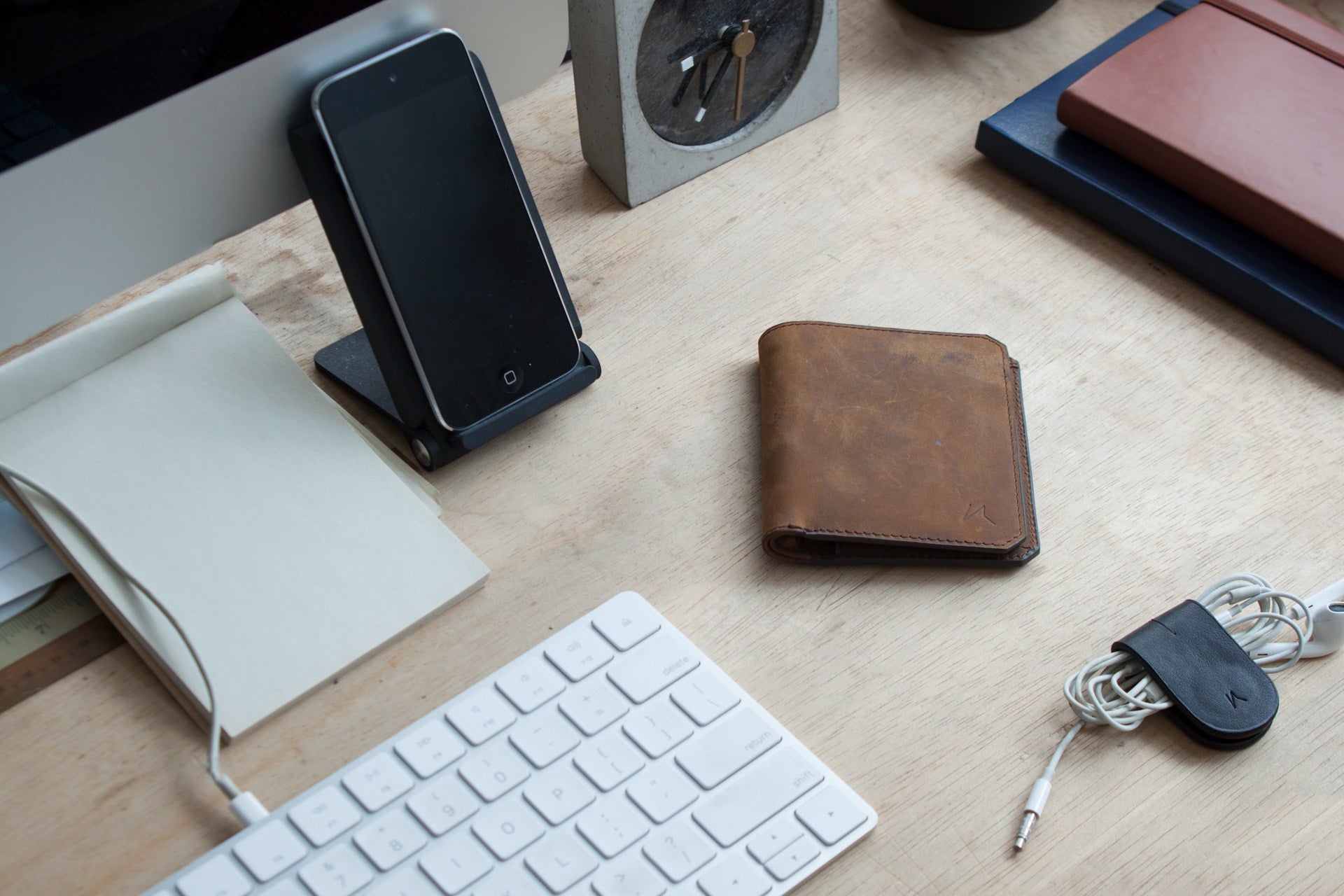 A table full of slim technology and notebooks, as well as a bifold wallet.