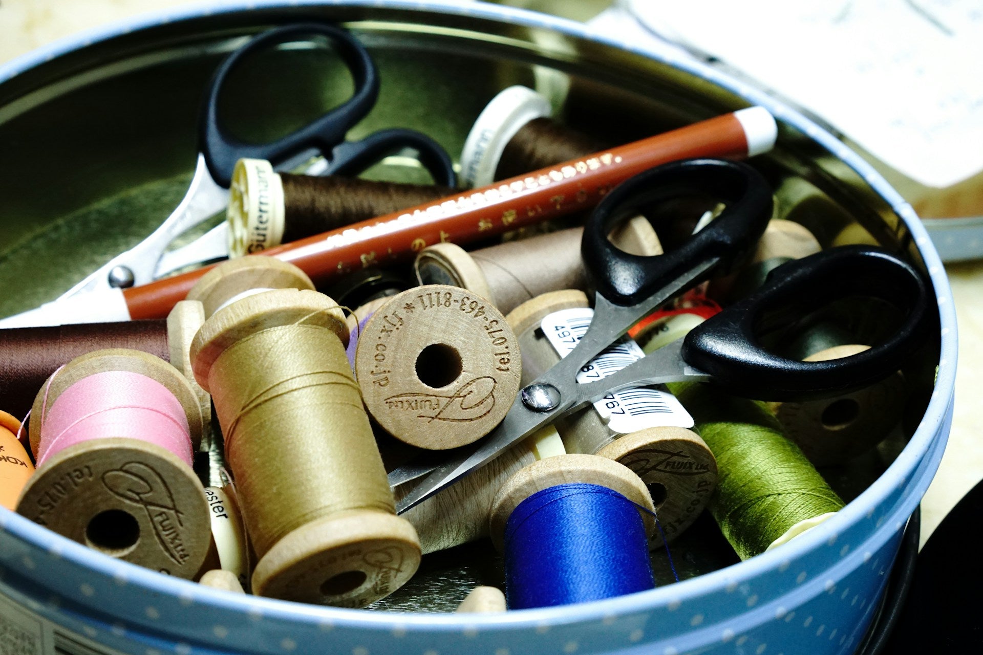 Various sewing supplies including thread and scissors in a small round tin.