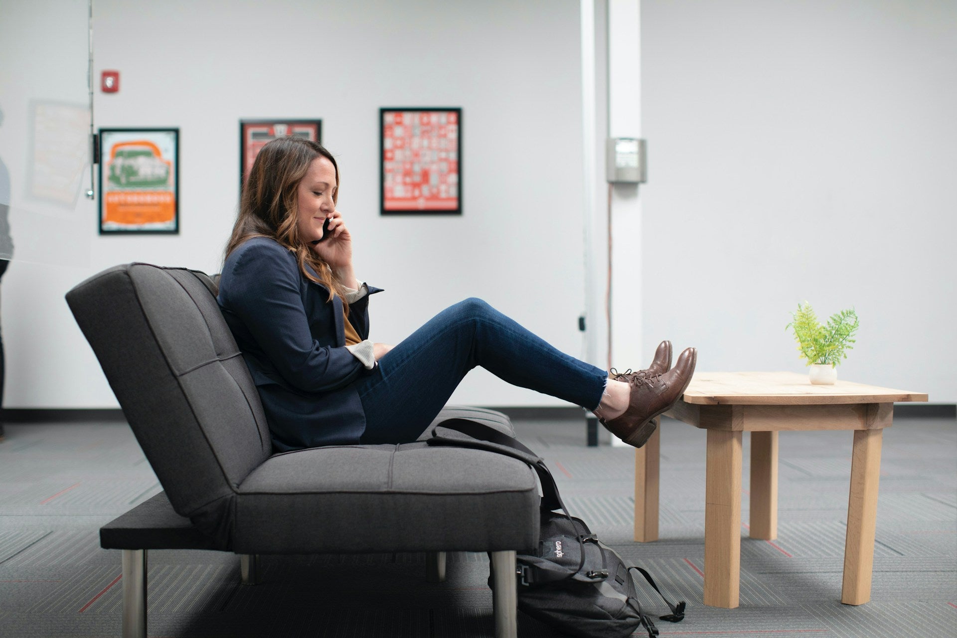 A woman in a suit sits on a sofa and talks on the phone.