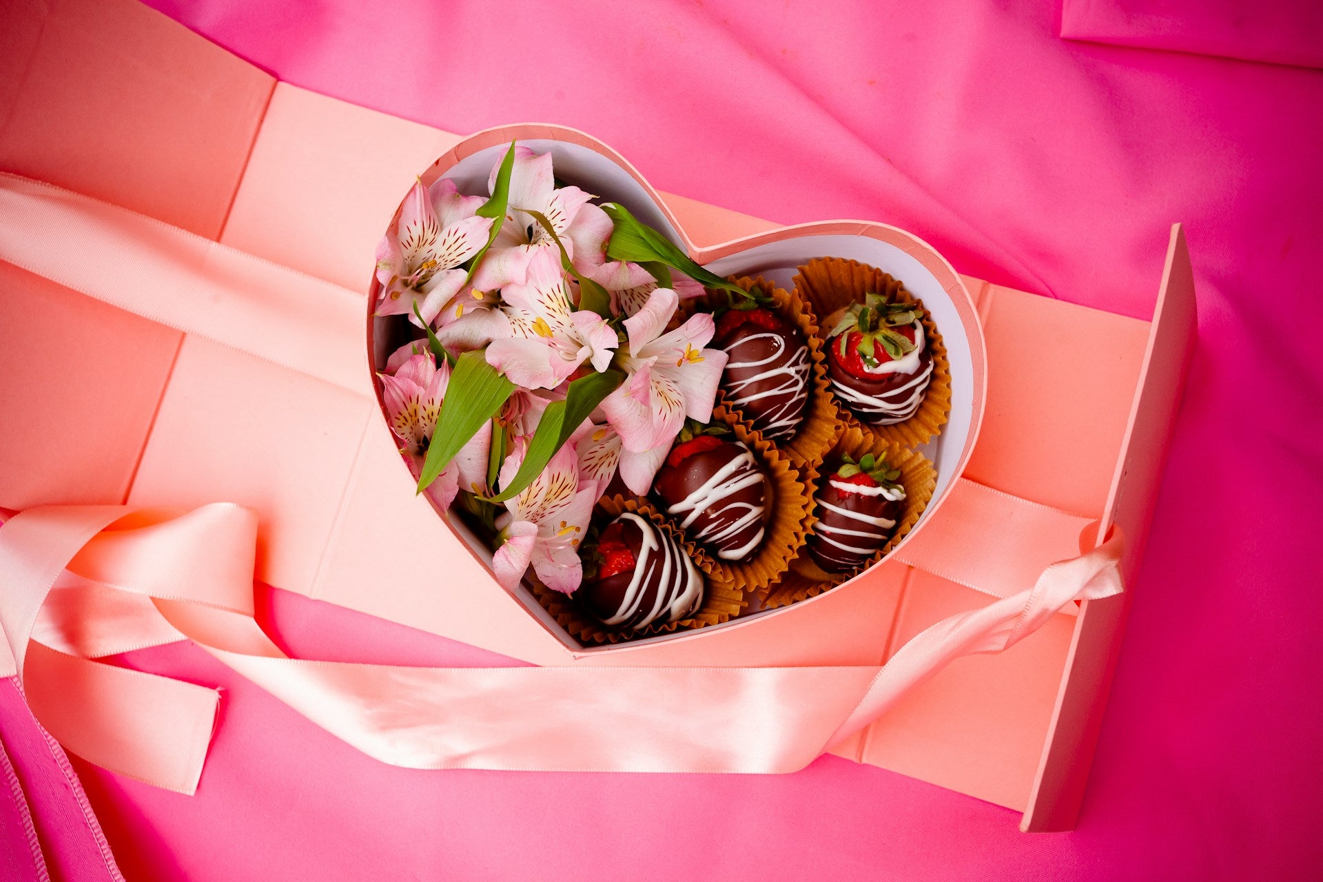 A heart-shaped box of chocolate covered strawberries and pink flowers.