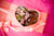 A heart-shaped box of chocolate covered strawberries and pink flowers.