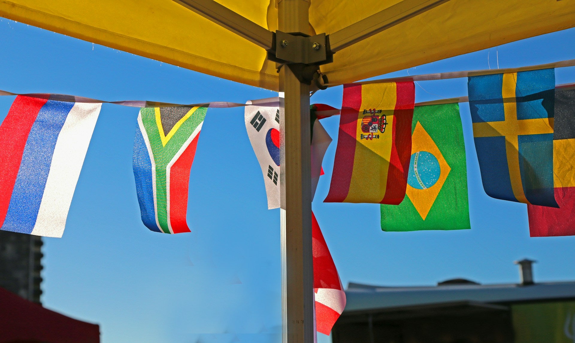 Several countries' flags hanging from bunting outside of a tent.