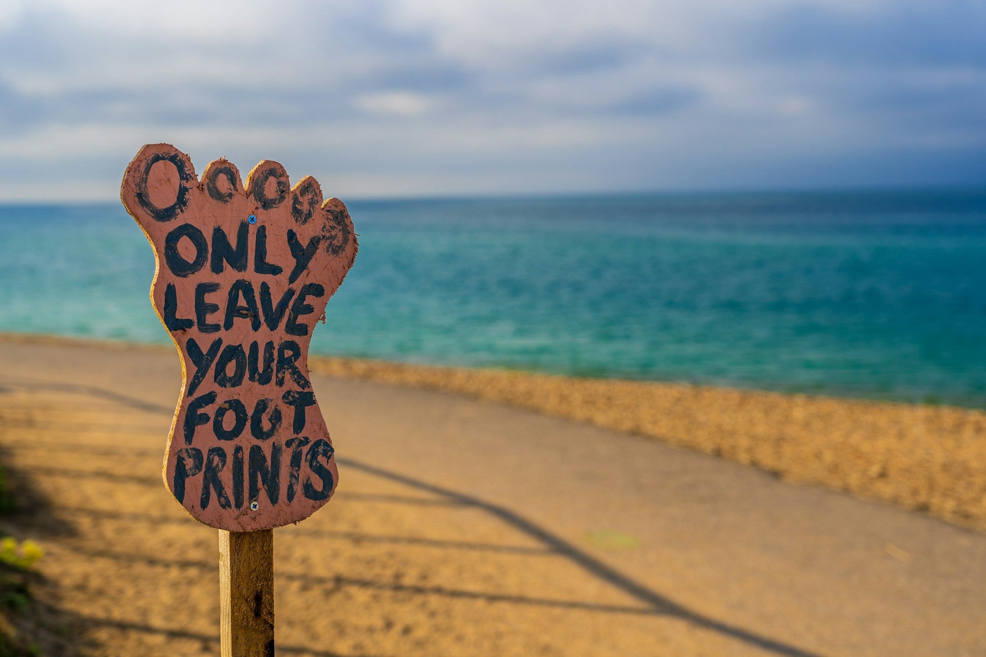 A beach at sunset with a foot-shaped sign that reads"Only Leave Your Footprints."