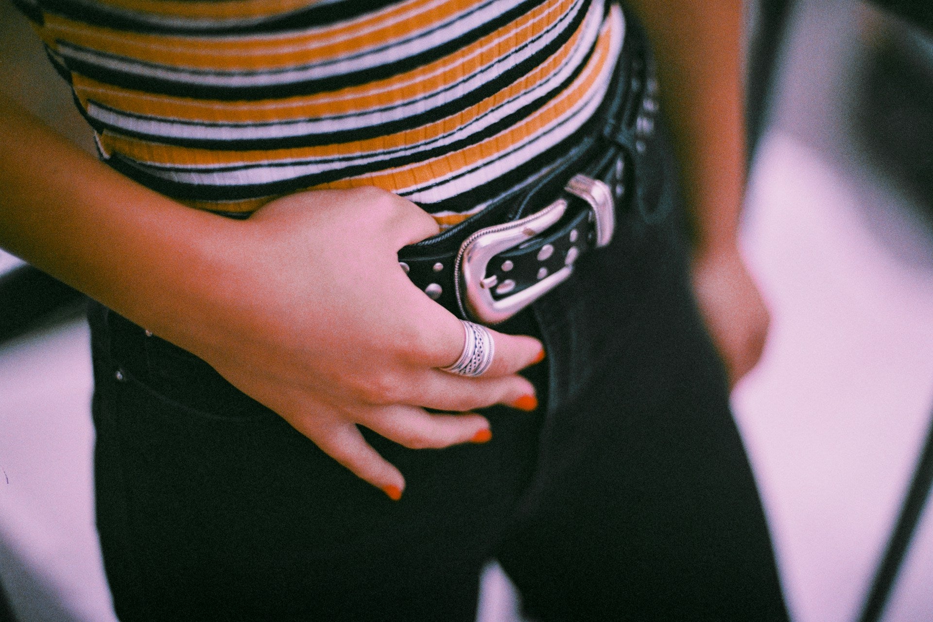 A woman wears black jeans with a studded black belt and a striped close-fitting top.