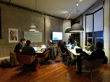 Office workers sit at tables angled toward a presentation screen in a room decorated in a modern style.