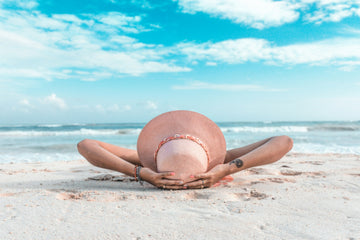 A shot from behind the head of a woman with a large sunhat lying on a beach. 