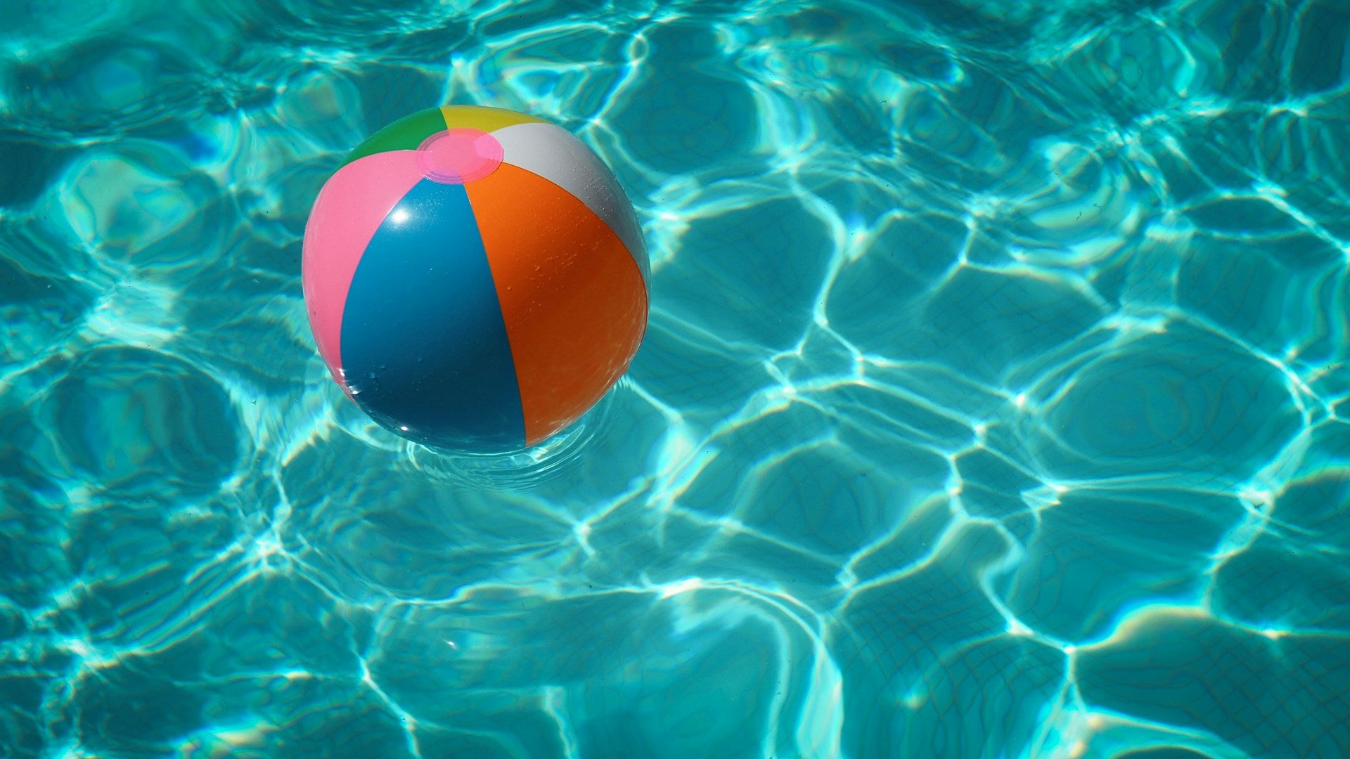 A colorful beach ball floating in pool water.