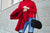 A woman in a red sweater, holding a red coat and black bag with a silver chain.