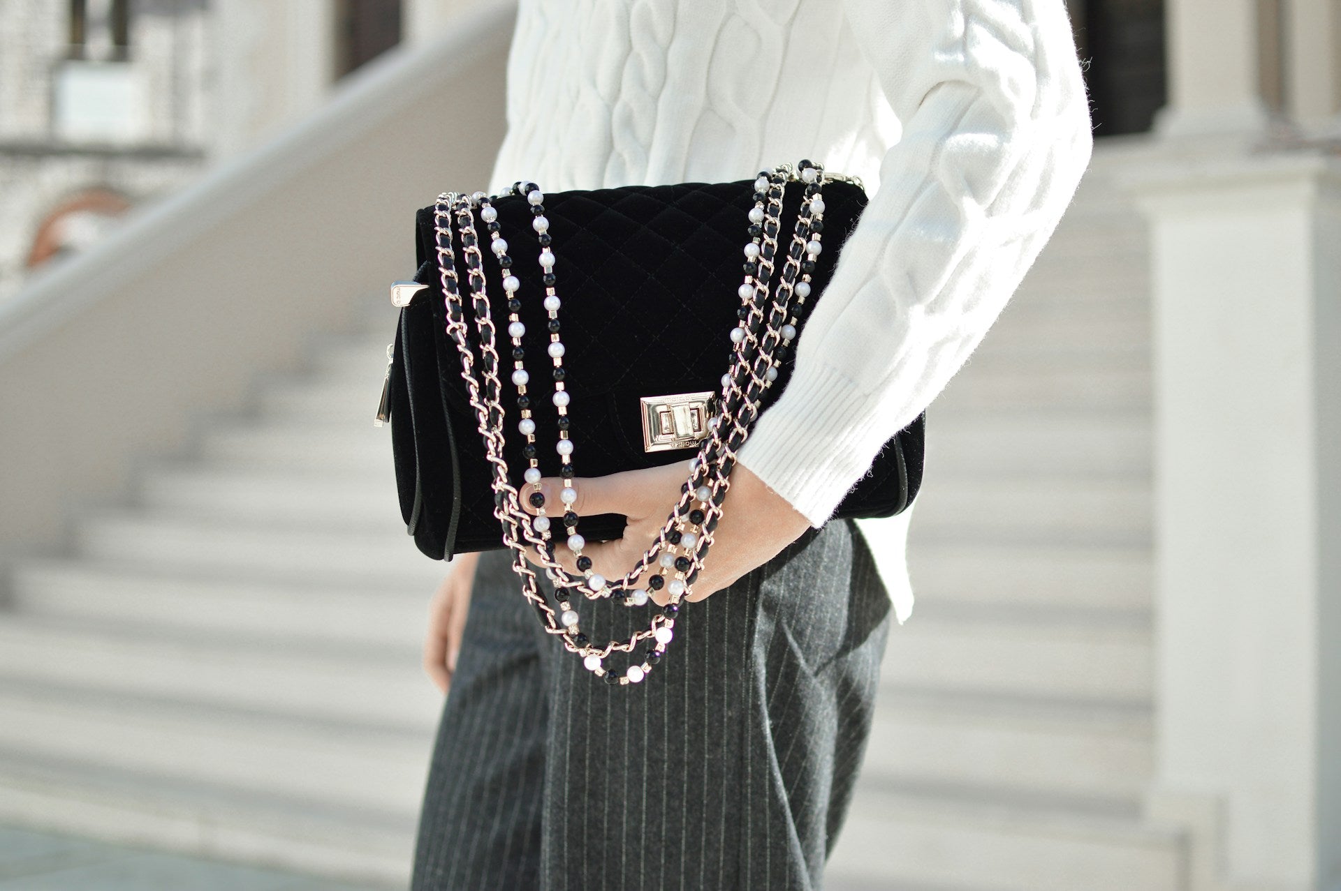 A woman holds a black leather shoulder purse with multiple chains.